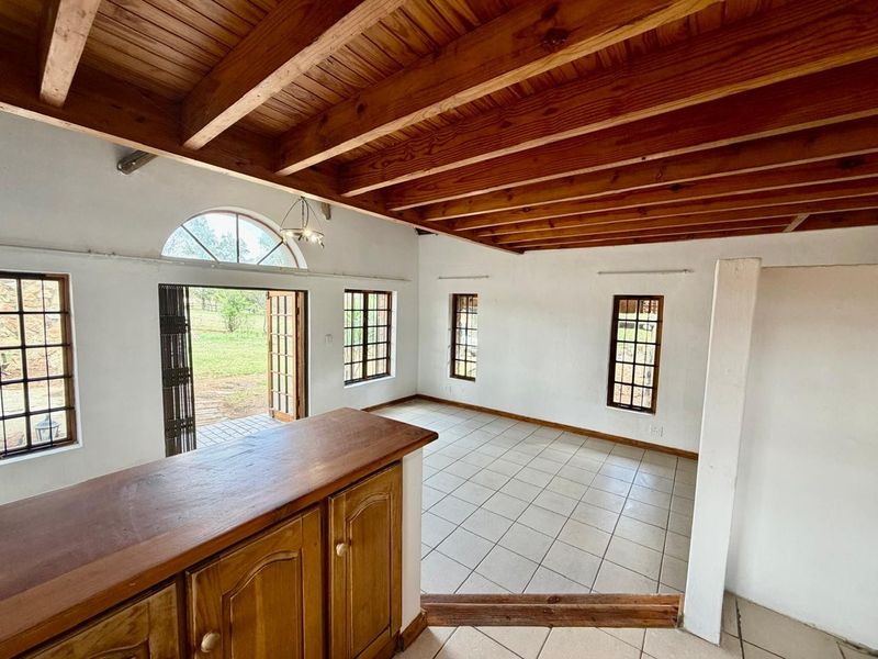 Spacious open-plan living area featuring exposed timber ceiling beams, tiled flooring, and large windows providing natural light and garden access.