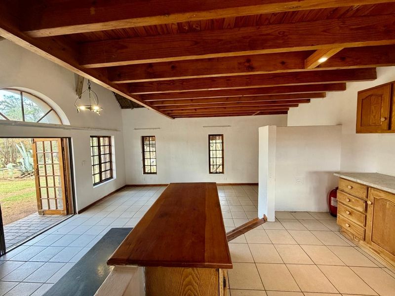 Spacious open-plan living area featuring exposed timber ceiling beams, tiled flooring, and direct access to the garden through classic french doors.