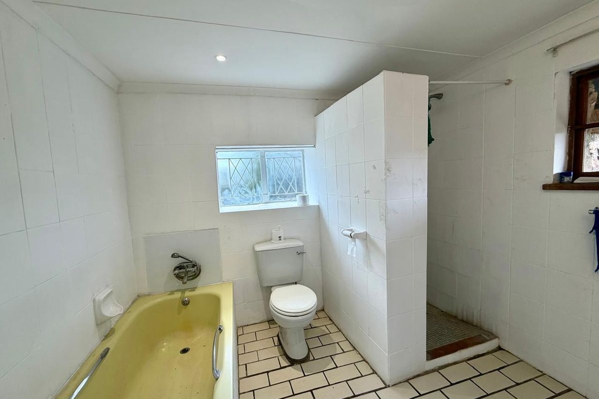 A functional bathroom featuring a bathtub, separate shower enclosure, and toilet, with white tiled finishes throughout.