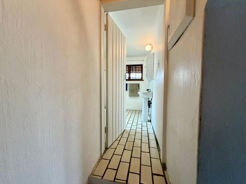 A narrow hallway leading into a bathroom area featuring a pedestal sink and tiled flooring.