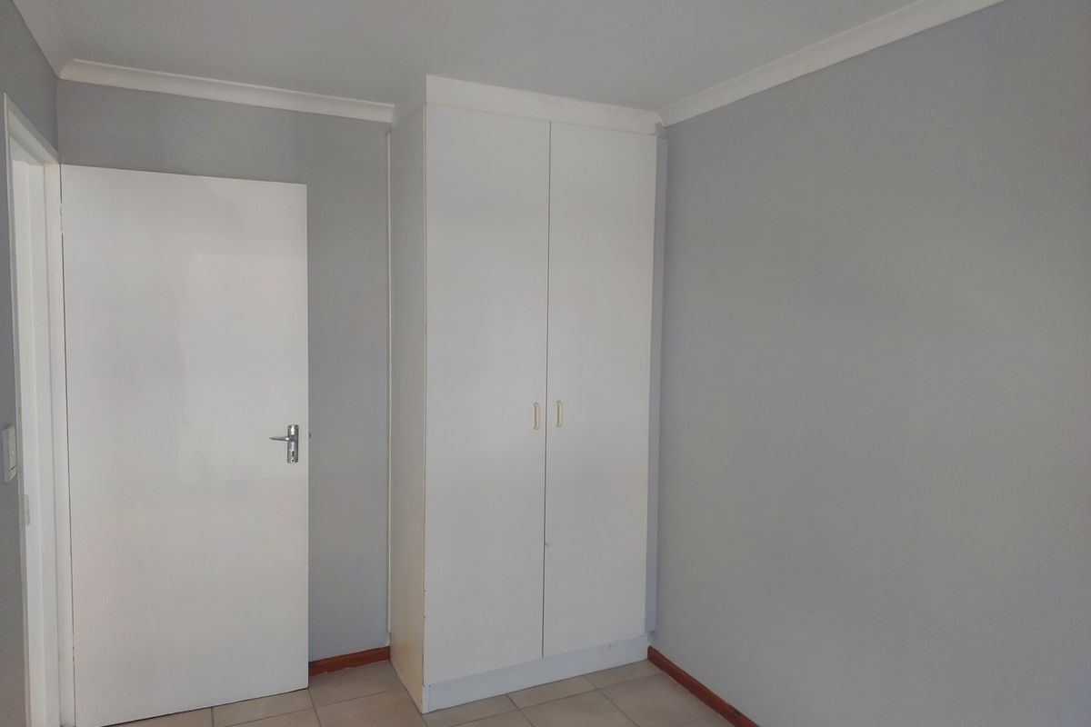 A clean, empty bedroom featuring neutral grey walls, tiled flooring, and a white built-in wardrobe.