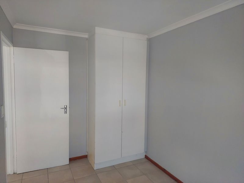 A clean, empty bedroom featuring neutral grey walls, tiled flooring, and a white built-in wardrobe.
