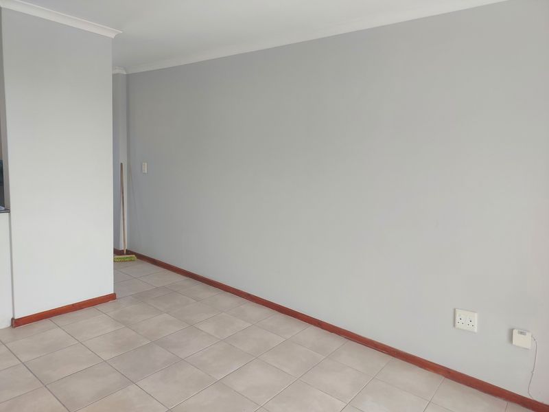 A bright, empty living area featuring neutral grey walls, tiled flooring, and timber skirting boards, providing a clean canvas for interior design.