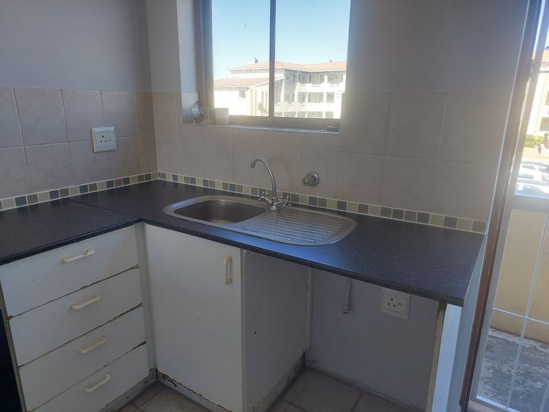 A compact kitchen area featuring laminate countertops, a stainless steel sink, and tiled backsplash, currently in need of cosmetic updates to the cabinetry.