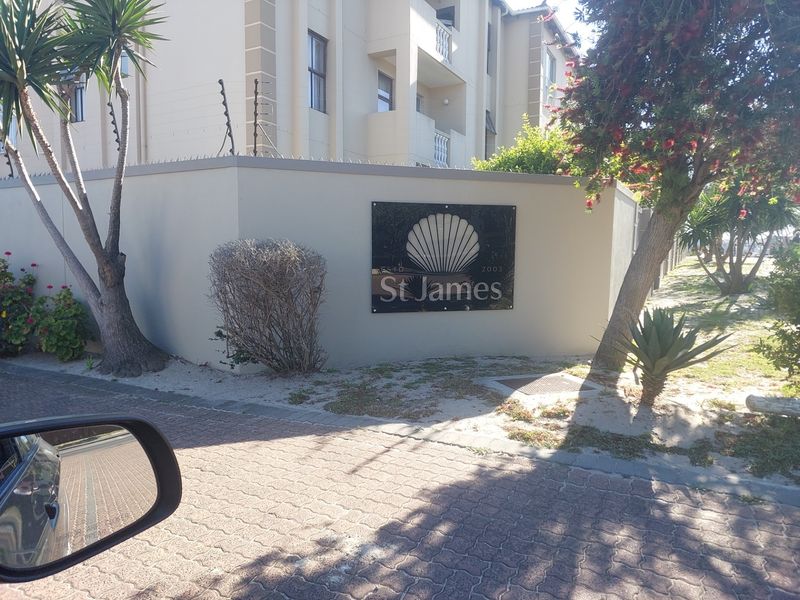 Street-level view of the St James apartment complex entrance, featuring a perimeter wall with electric fencing and paved driveway access.