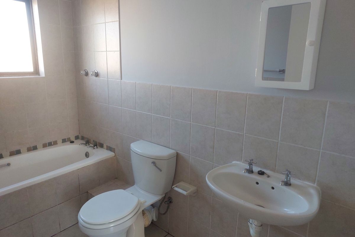 A functional bathroom featuring a bathtub with shower head, wall-mounted basin, and toilet, finished with neutral wall and floor tiles.