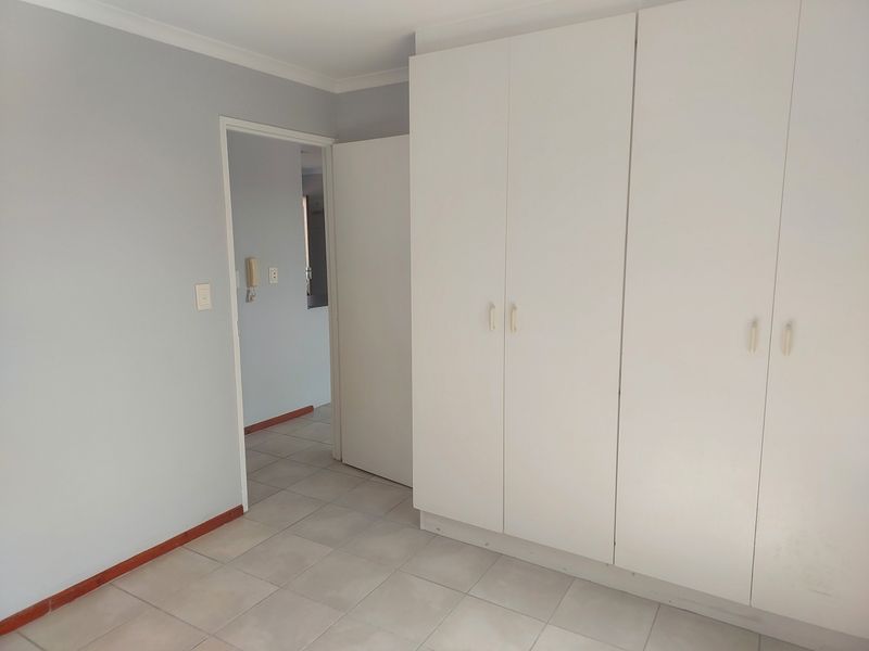 A clean, empty bedroom featuring neutral tiled flooring and white built-in cupboards, offering a blank canvas for personalization.