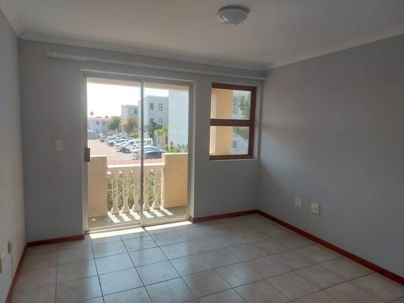 An empty, well-lit living area featuring neutral tiled floors, a sliding glass door leading to a balcony, and clean wall finishes.