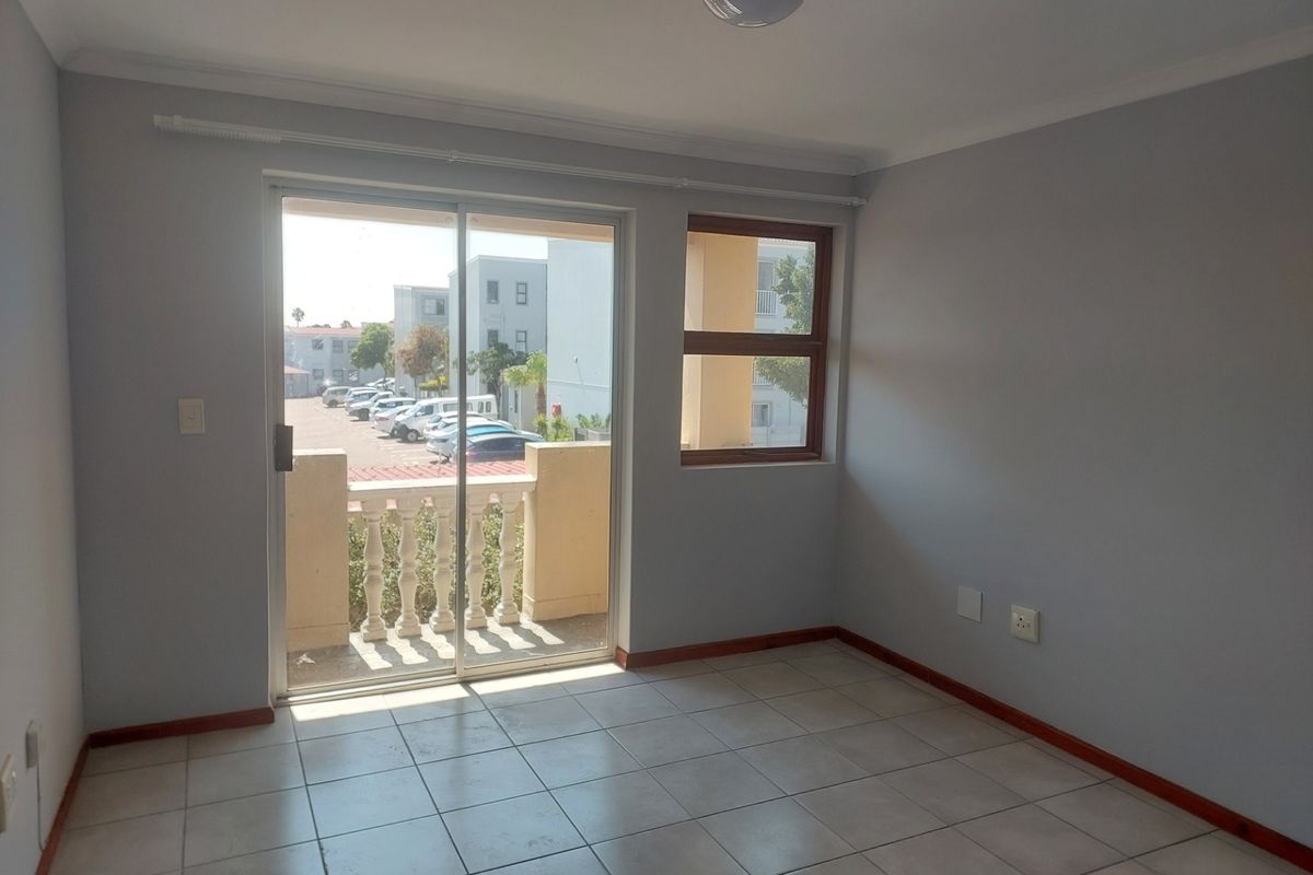 An empty, well-lit living area featuring neutral tiled floors, a sliding glass door leading to a balcony, and clean wall finishes.