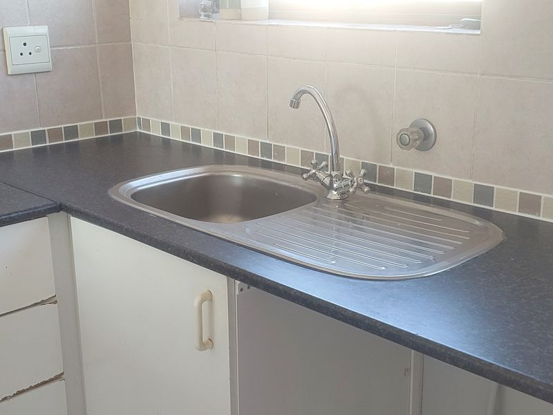 A functional kitchen area featuring a stainless steel sink, dark laminate countertops, and tiled backsplash with built-in cabinetry.