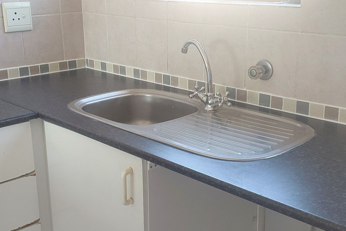 A functional kitchen area featuring a stainless steel sink, dark laminate countertops, and tiled backsplash with built-in cabinetry.