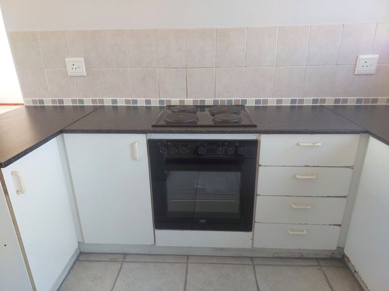 A functional kitchen area featuring a built-in oven, electric hob, tiled backsplash, and white cabinetry with visible wear on the drawer edges.