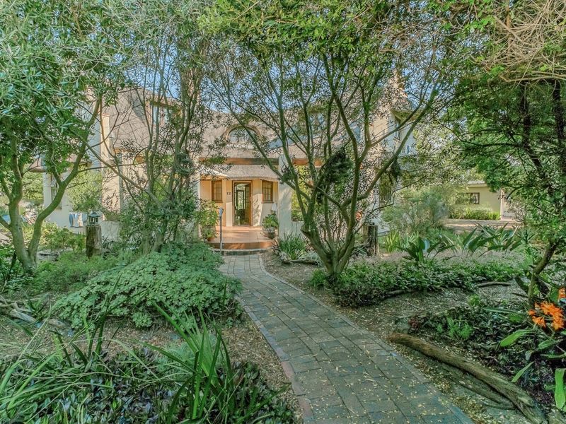 A charming house exterior featuring a thatched roof, a welcoming covered entrance porch, and a well-established landscaped garden with a brick pathway.