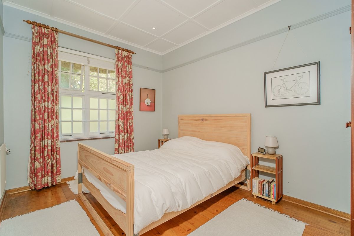 A well-maintained bedroom featuring warm timber flooring, a classic paneled ceiling, and a multi-pane window with a traditional picture rail.