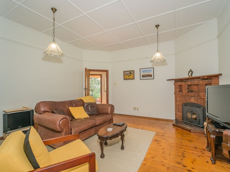 A cozy living room featuring original timber flooring, a classic brick fireplace with a wood-burning stove, and a distinctive coffered ceiling.