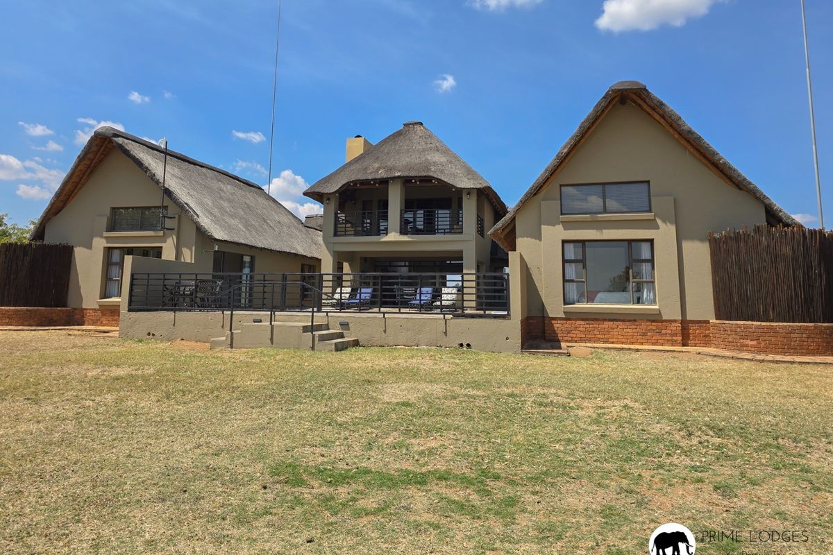 Rear view of a multi-structure property featuring traditional thatch roofing, brick base detailing, and a spacious raised patio area overlooking the garden.