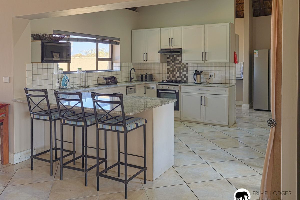 A functional kitchen featuring granite countertops, a breakfast bar, built-in cabinetry, and a gas hob with an extractor fan.