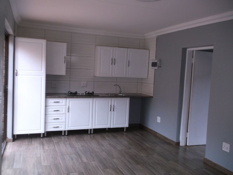 A clean, modern kitchen featuring white cabinetry, dark laminate countertops, a built-in gas hob, and wood-look floor tiles in an open-plan layout.