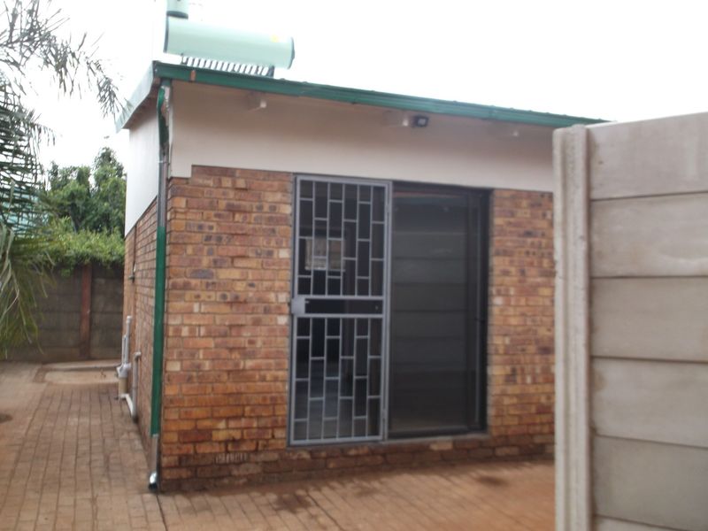 Rear view of the cottage featuring face brick construction, a solar water heater, paved patio area, and secure sliding door access.