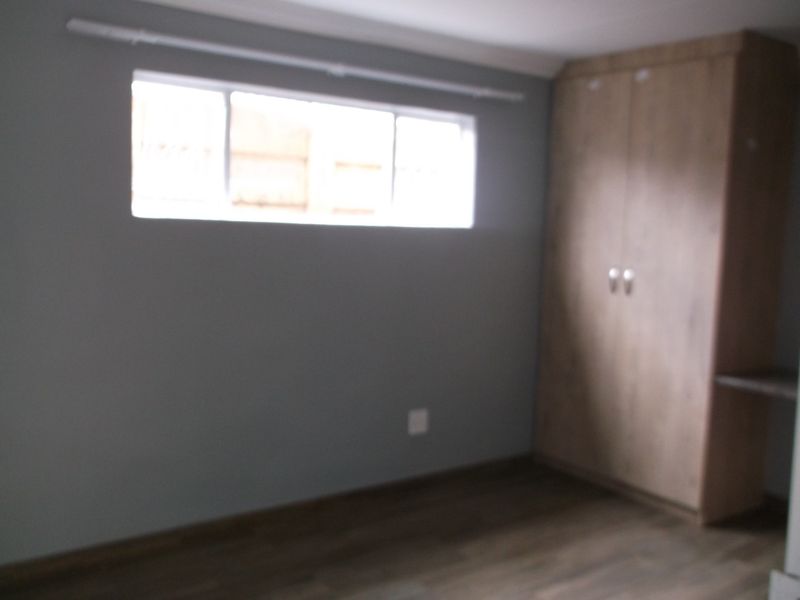A simple bedroom featuring laminate flooring, a built-in wardrobe, and a horizontal window, providing a clean and functional space.