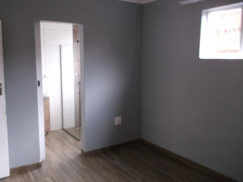 A clean, empty bedroom featuring modern grey walls, wood-look laminate flooring, and an adjoining en-suite bathroom.