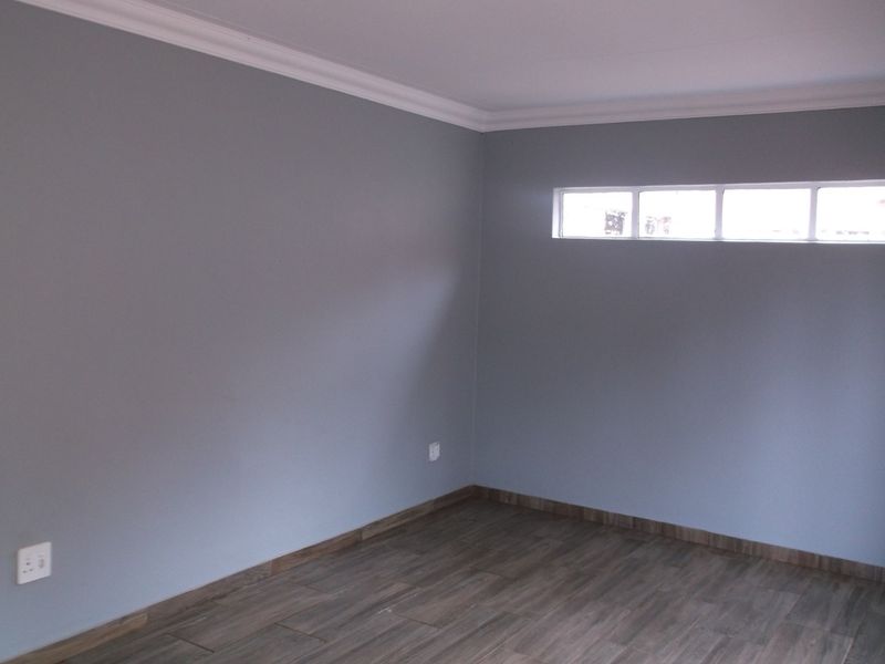 A clean, empty bedroom featuring modern grey walls, wood-look laminate flooring, and a high-set horizontal window for natural light.