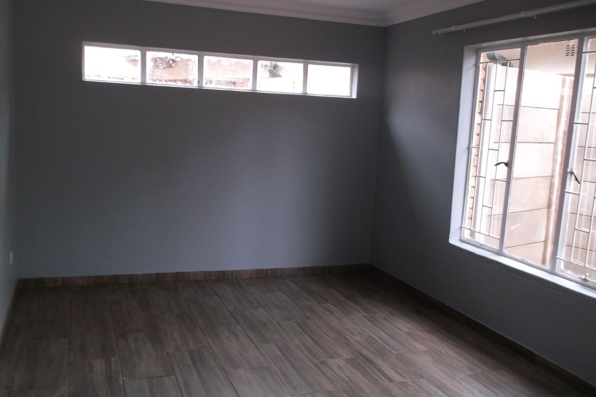 A bright, empty bedroom featuring wood-look tile flooring, neutral grey walls, and security-fitted windows, offering a clean and modern blank canvas.