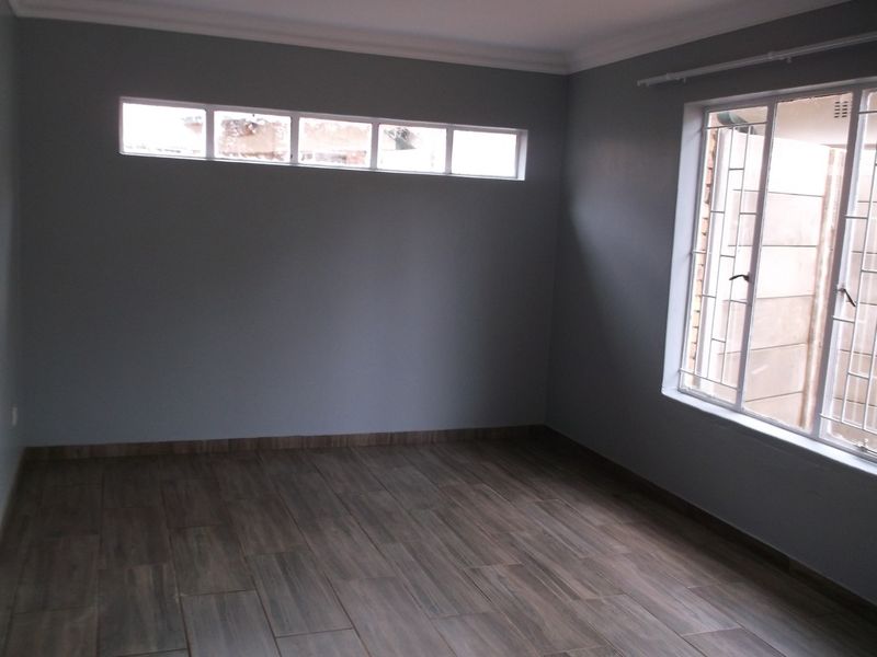 A bright, empty bedroom featuring wood-look tile flooring, neutral grey walls, and security-fitted windows, offering a clean and modern blank canvas.