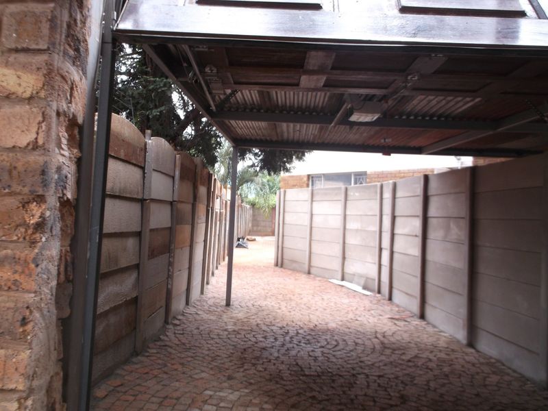 A covered outdoor parking area featuring a corrugated metal roof, brick paving, and precast concrete boundary walls.
