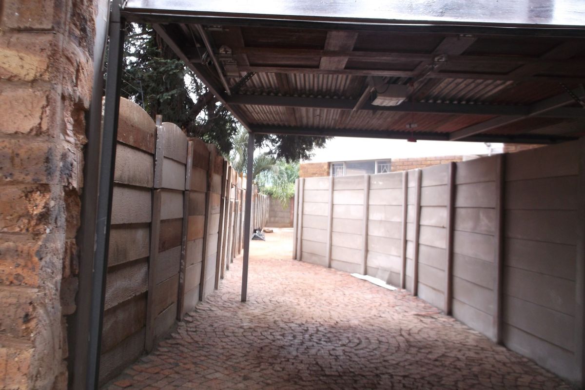 A covered outdoor parking area featuring a corrugated metal roof, brick paving, and precast concrete boundary walls.