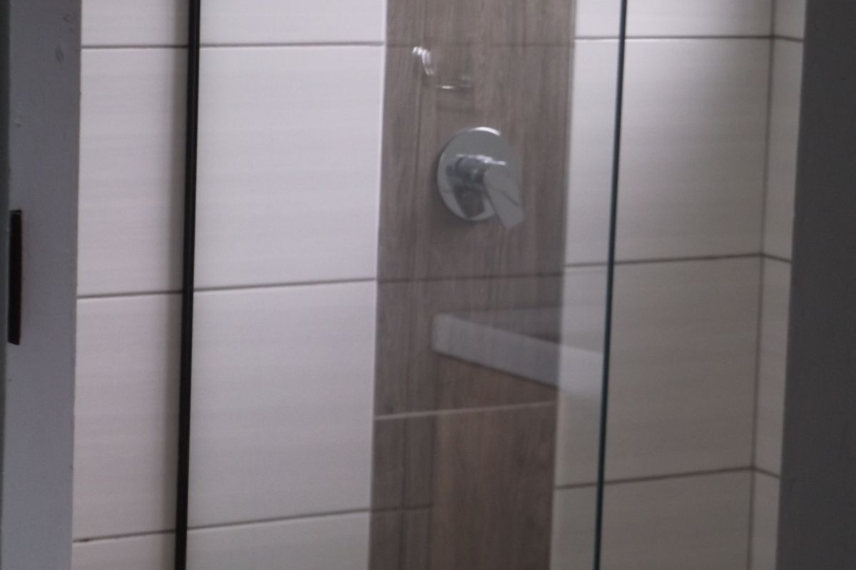 A close-up view of a modern shower enclosure featuring a glass screen, chrome mixer tap, and contemporary wood-look and white wall tiling.