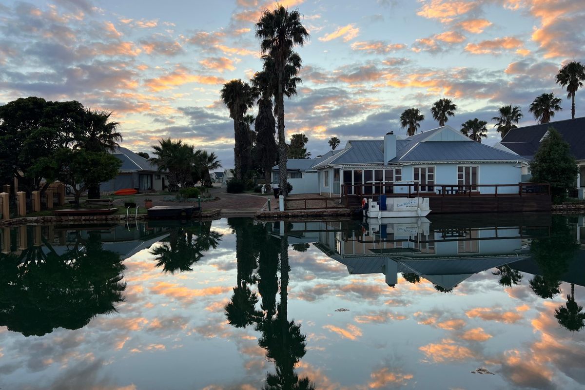 A scenic rear view of a waterfront residential property featuring a timber deck, metal roofing, and established palm trees at sunset.