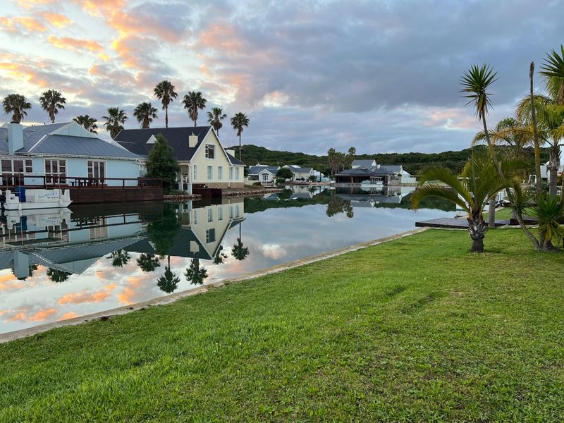 A scenic view of a tranquil canal with waterfront residential properties, manicured lawns, and mature palm trees under a sunset sky.