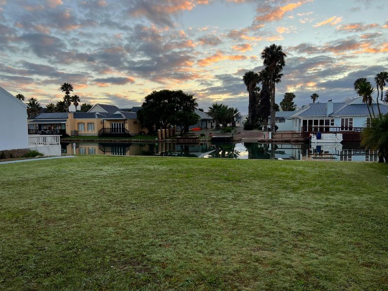 A scenic view of a tranquil waterfront residential area featuring manicured lawns, mature palm trees, and surrounding homes at sunset.