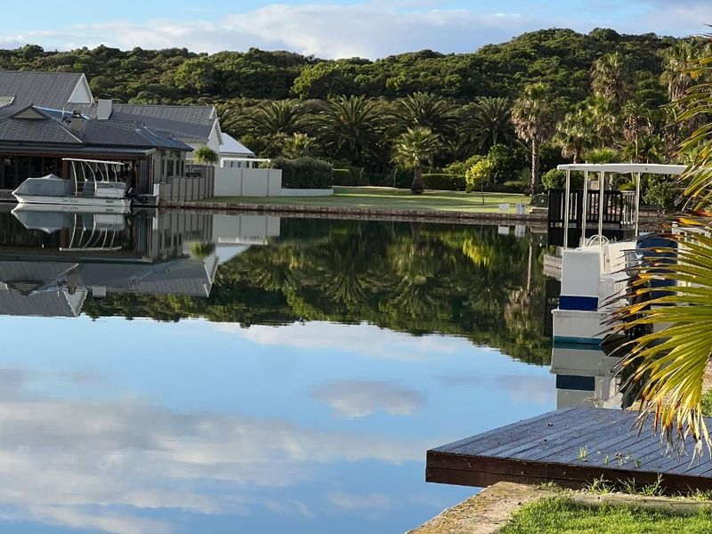 A scenic view of a tranquil canal with a private jetty, manicured lawn, and surrounding lush landscape.