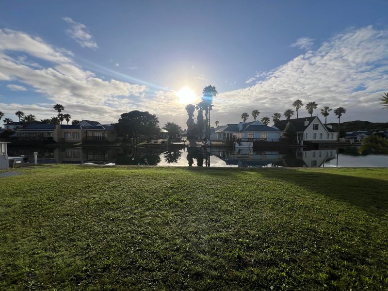 A scenic view of a tranquil waterfront area with manicured lawns and surrounding residential properties under a bright sky.
