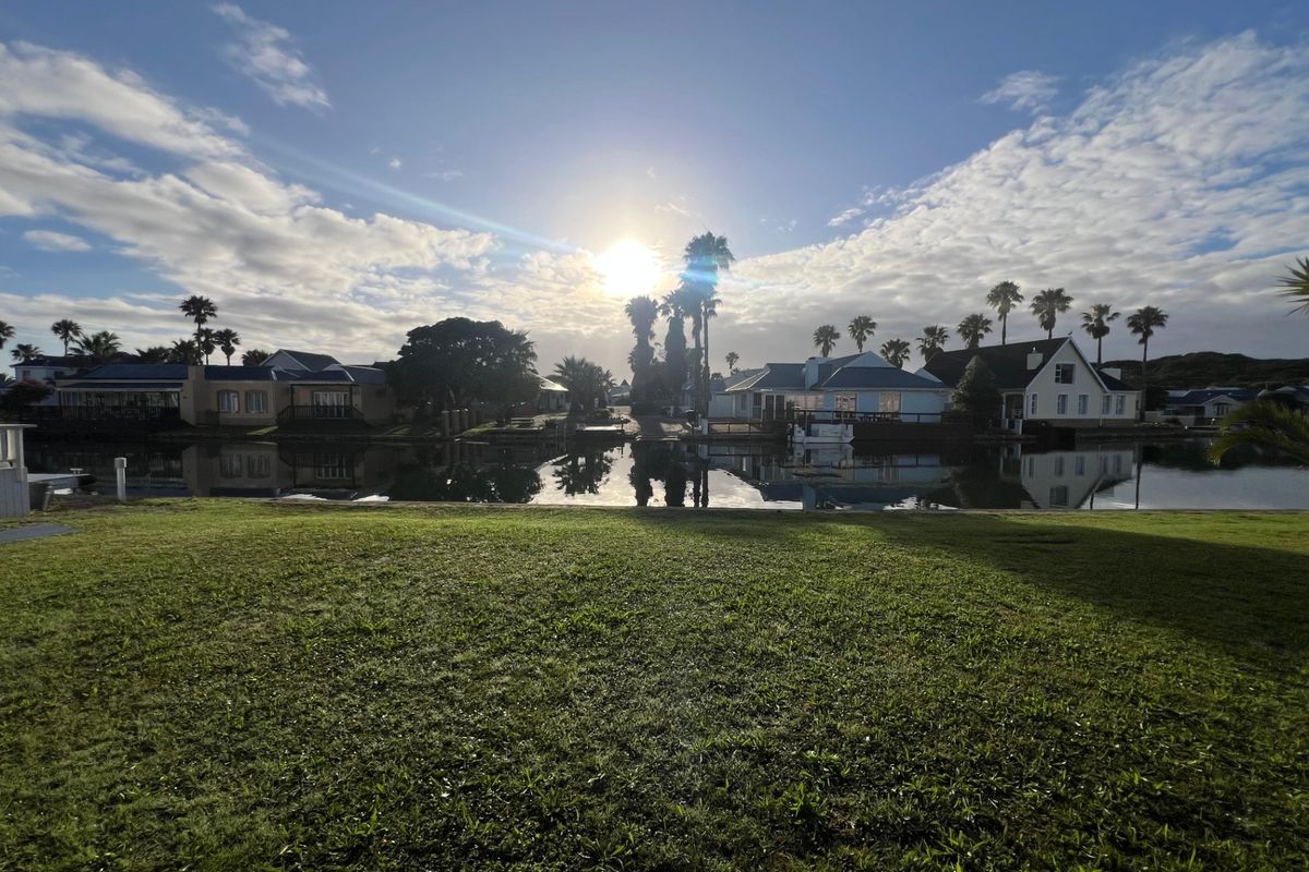 A scenic view of a tranquil waterfront area with manicured lawns and surrounding residential properties under a bright sky.