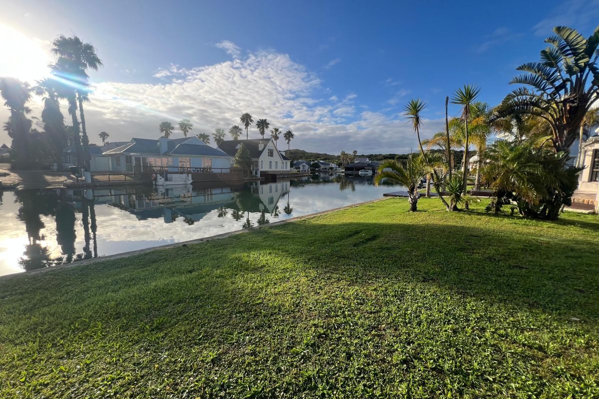 A scenic view of a tranquil canal waterfront featuring manicured lawns and mature palm trees, showcasing the peaceful residential estate setting.