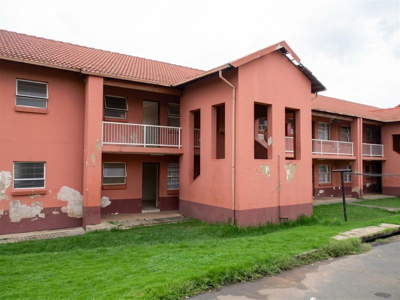 Exterior view of a multi-story residential building featuring terracotta roof tiles, balconies with metal railings, and visible exterior wall maintenance requirements.