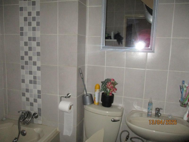 A functional bathroom featuring tiled walls with a mosaic accent, a pedestal sink, a toilet, and a bathtub with a shower mixer.