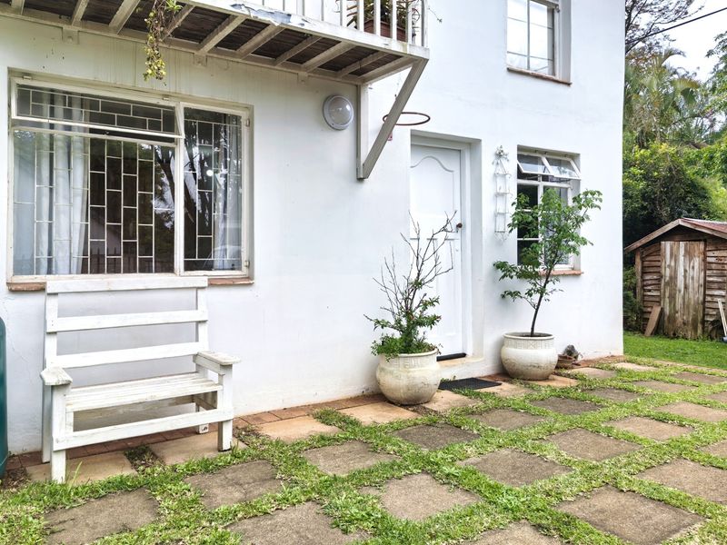 Rear exterior view of the cottage featuring a paved patio area, security bars on windows, a small balcony, and a detached timber garden shed.