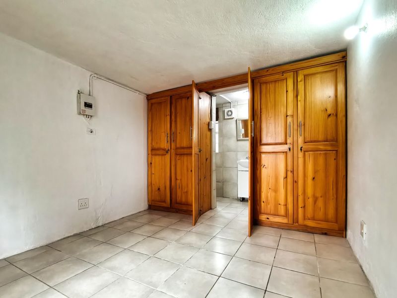 A bedroom featuring built-in wooden cupboards, tiled flooring, and direct access to an en-suite bathroom area.