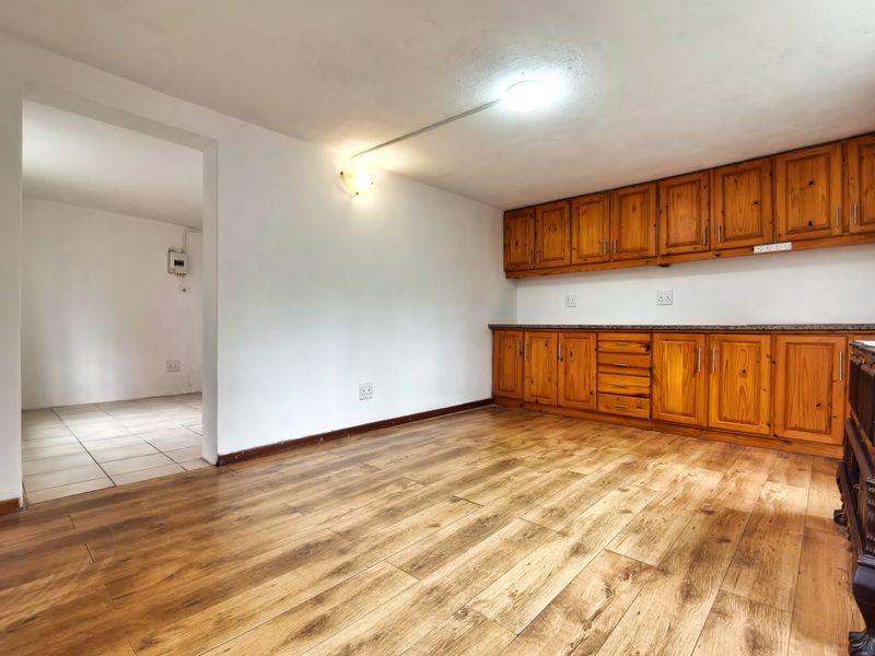 A functional kitchen area featuring wooden cabinetry, stone countertops, and laminate flooring, with an adjacent tiled utility space.