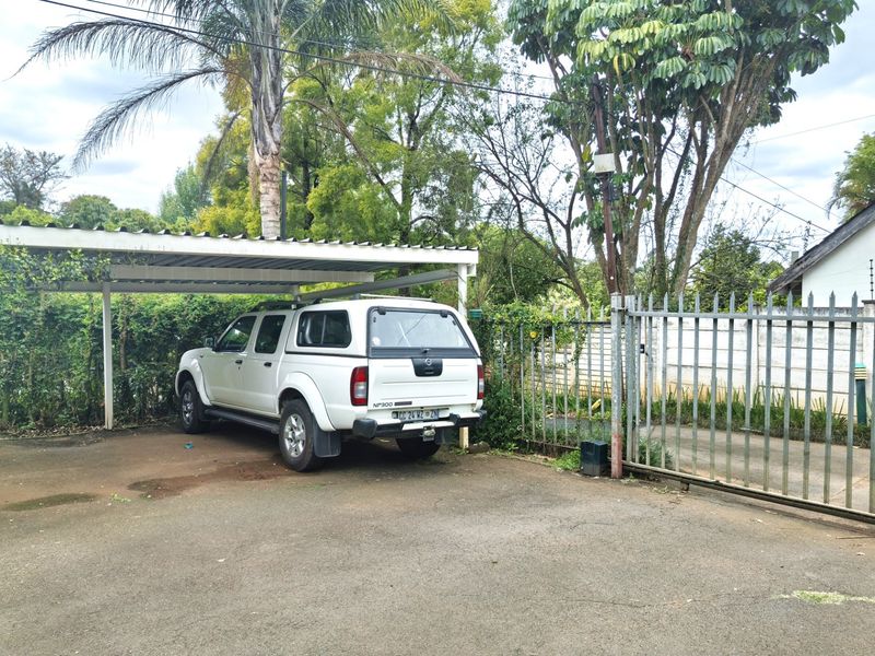 A functional outdoor carport area with metal fencing and paved driveway, providing covered parking space on the property.