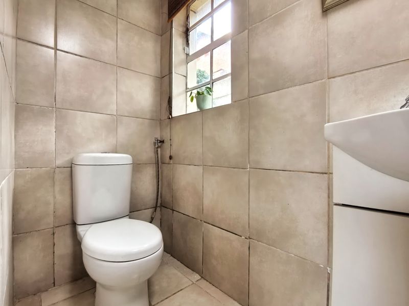 A compact bathroom featuring neutral ceramic wall and floor tiles, a standard toilet, and a wall-mounted basin.