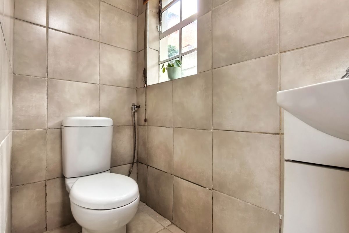 A compact bathroom featuring neutral ceramic wall and floor tiles, a standard toilet, and a wall-mounted basin.