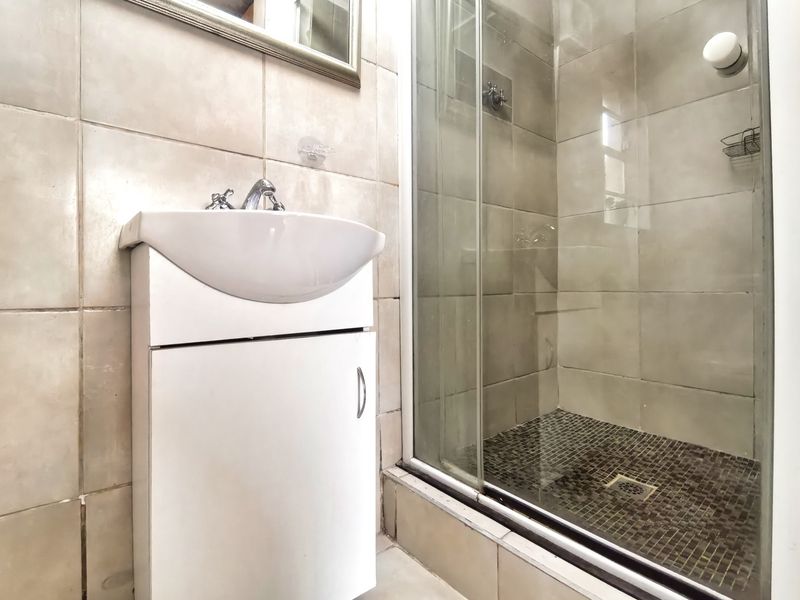 Compact bathroom featuring a white vanity cabinet with basin and a glass-enclosed shower with tiled finishes.