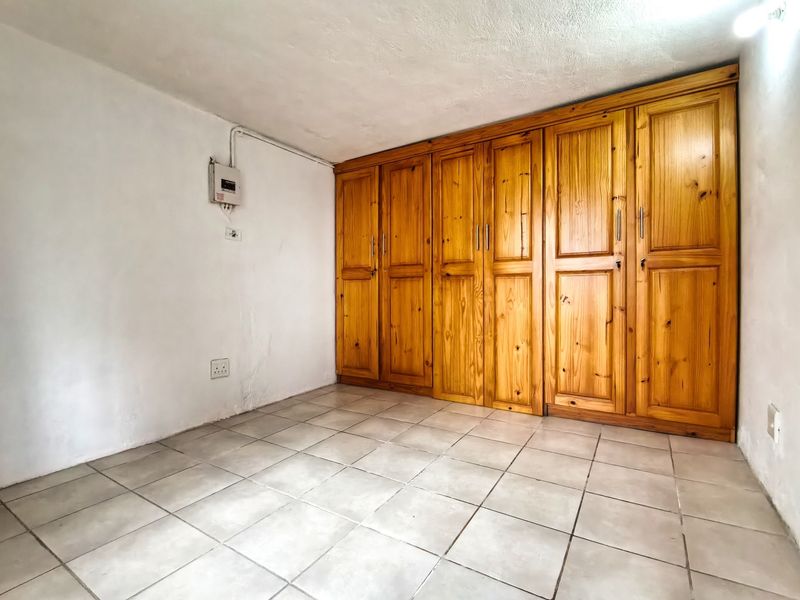 An empty bedroom featuring tiled flooring and extensive built-in wooden cabinetry, providing ample storage space.