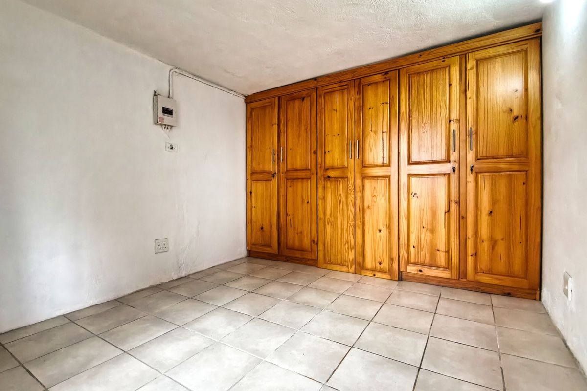 An empty bedroom featuring tiled flooring and extensive built-in wooden cabinetry, providing ample storage space.