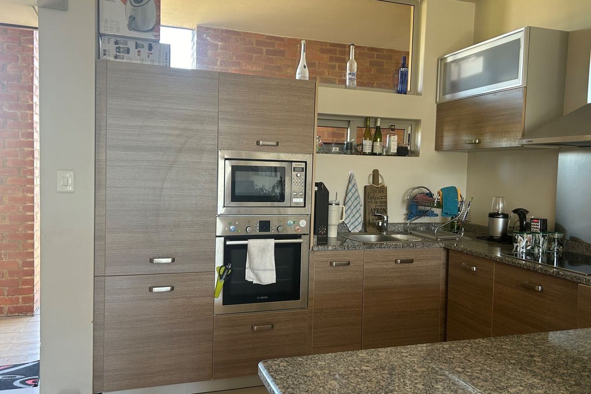 A functional kitchen featuring wood-finish cabinetry, granite countertops, built-in oven and microwave, and a stainless steel sink, with an open-plan layout.